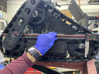 Gloved hand holds a red measuring bar across the side of the raised tread assembly.