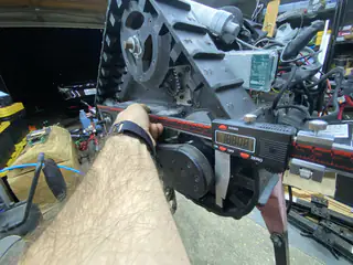 Wider angled view shows a hand holding a digital caliper across the tread frame beside exposed electronics.