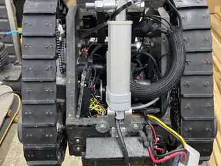Rear view between both treads showing a central linear actuator, hoses, and wiring.