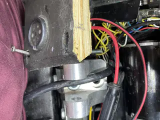 Wooden spacer and metal pivot hardware fitted beside internal wiring and the chassis wall.