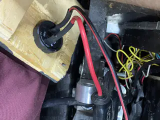 Red and black power cables pass through a sealed fitting in a wooden mounting block.