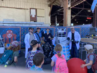 Presenters stand between two robots as children watch from the front of the booth.