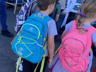 Two children with bright backpacks lean forward for a closer look at the demonstration.