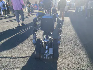 Close rear view of R.O.B. centered on the sunlit midway among surrounding visitors.
