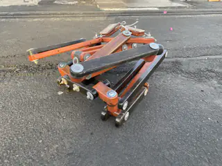 Compact orange articulated rover with linked arms and small wheels rests on the pavement.
