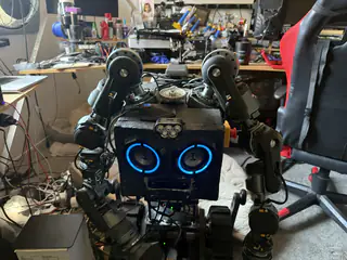 Front view of R.O.B. with blue speaker eyes, raised shoulder joints, and exposed wiring.