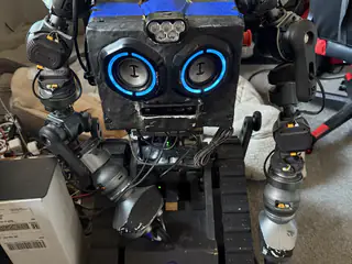 Centered front view of R.O.B. with both articulated arms hanging beside the illuminated speaker face.