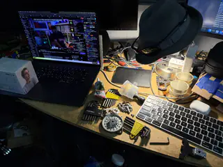 Slightly wider workbench view showing the laptop, lamp, keyboard, loose hardware, and circular gear assembly.