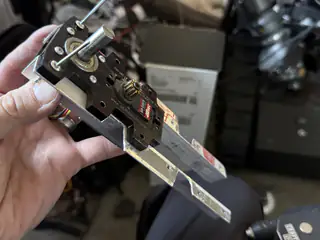 Hand holding a black servo-and-bracket assembly beside R.O.B.’s arm joints.