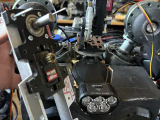 Hand positioning a shafted servo bracket in front of R.O.B.’s central gear assembly.