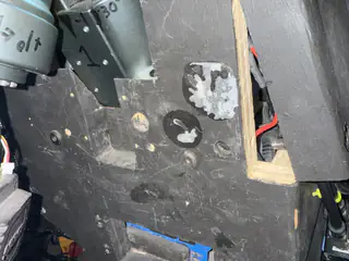 Worn black side panel with circular scuffs, exposed wood, and part of an arm joint.