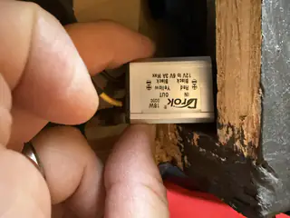 Hand holding a small silver electronic module inside the robot’s wooden frame.