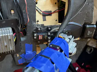 Slightly wider front view of the taped arm mechanism, exposed chest switch, wiring, and rough wooden opening.