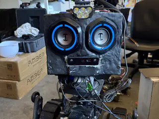 Close frontal portrait of R.O.B.’s blue speaker eyes, forehead light, and exposed lower wiring.