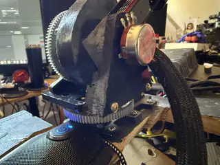 Angled close-up of a round metal motor cap, bolts, braided cables, and blue-lit base.