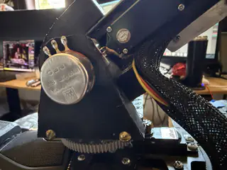 Closer side view of the circular motor cap, mounting bolts, braided cable sleeve, and lower gear.