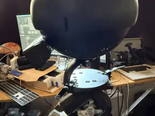 Underside of a black spherical camera head above a circular perforated neck plate.