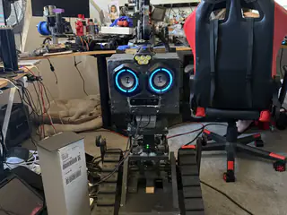 Full frontal view of R.O.B. with blue speaker eyes and spherical camera head in the workshop.