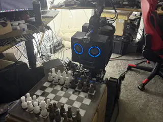 R.O.B. facing a chessboard filled with black and white pieces on stacked cardboard boxes.