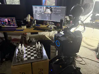 Side view of R.O.B. beside the chessboard, with laptop and large monitor screens behind.