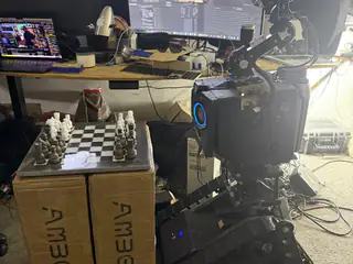 Wider rear-side view showing R.O.B., the chessboard on boxes, and multiple workshop monitors.