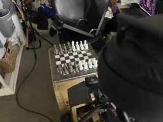 Overhead angle showing R.O.B.’s head and shoulder beside a chessboard on labeled boxes.