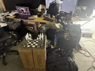 Wide side view of R.O.B. positioned next to the chessboard and cluttered computer workbench.
