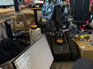 R.O.B. standing behind an angled laptop screen, with both articulated arms visible in the workshop.