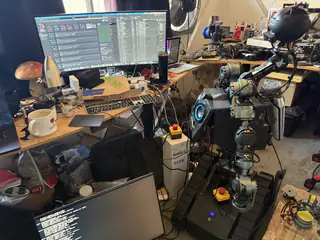 R.O.B. beside a monitor displaying development software, surrounded by tools and electronics.