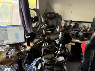 Rear three-quarter view of R.O.B.’s spherical camera head, neck joints, and upper arm beside a laptop.