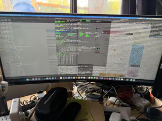 Ultrawide monitor showing multiple code, log, and table windows above a cluttered desk.