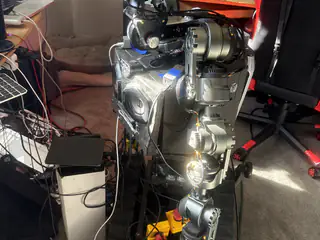 Brightly lit side view of R.O.B.’s torso, speaker face, articulated arm, and tracked base.
