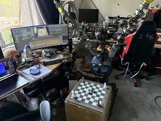 R.O.B. raises both articulated arms beside a chessboard while its control software runs on nearby screens.