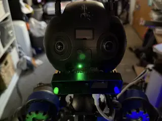 Close portrait of R.O.B.'s spherical camera head and antennas lit by green and blue light.