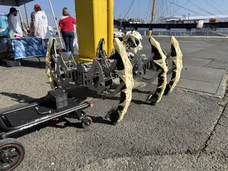 A skeletal quadruped robot prototype stands outdoors near the 2026 maker displays.